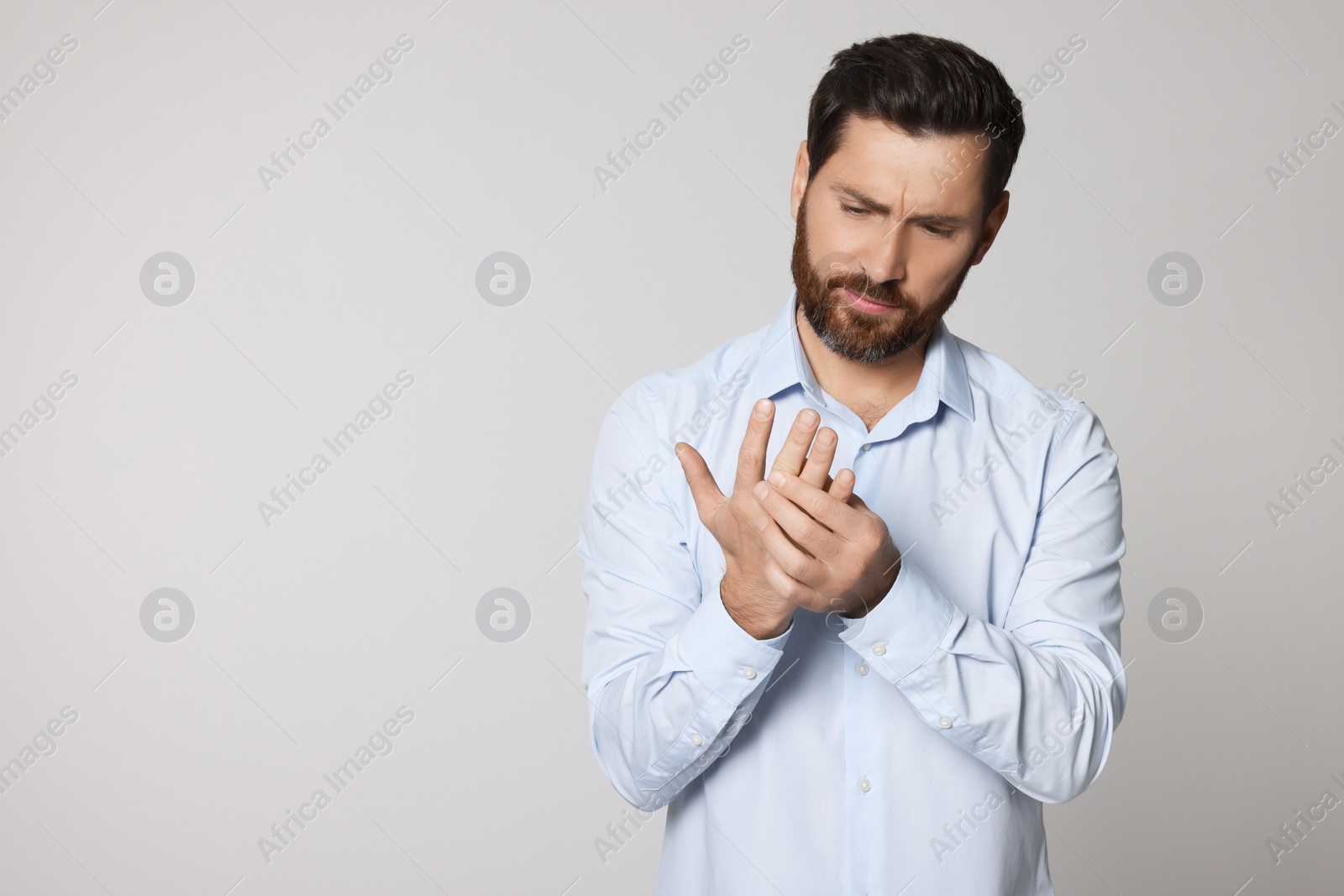 Photo of Man suffering from pain in his hand on light background, space for text. Arthritis symptoms