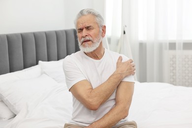 Arthritis symptoms. Man suffering from pain in shoulder on bed at home