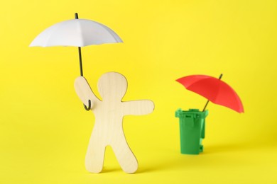 Wooden human figure holding white umbrella and red one in trash can on yellow background. Choosing better concept