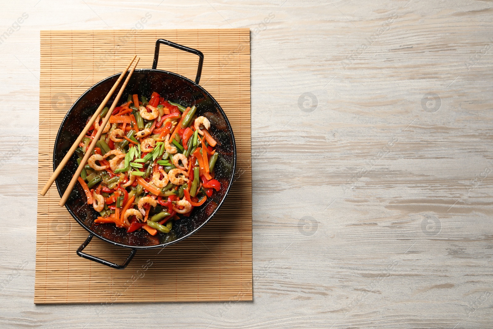 Photo of Shrimp stir fry with vegetables in wok and chopsticks on wooden table, top view. Space for text