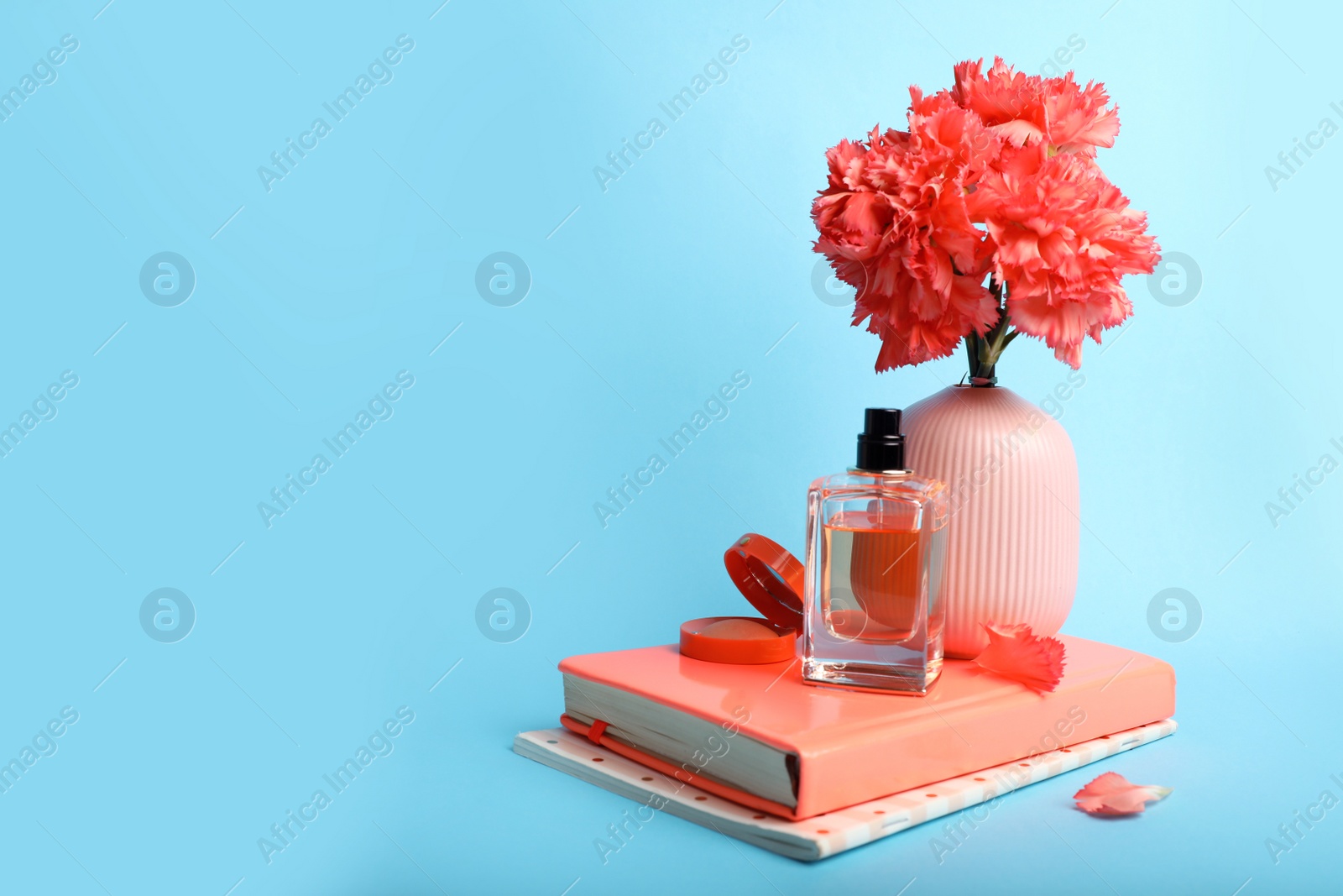 Photo of Composition with coral notebooks, flowers and perfume on light blue background. Space for text