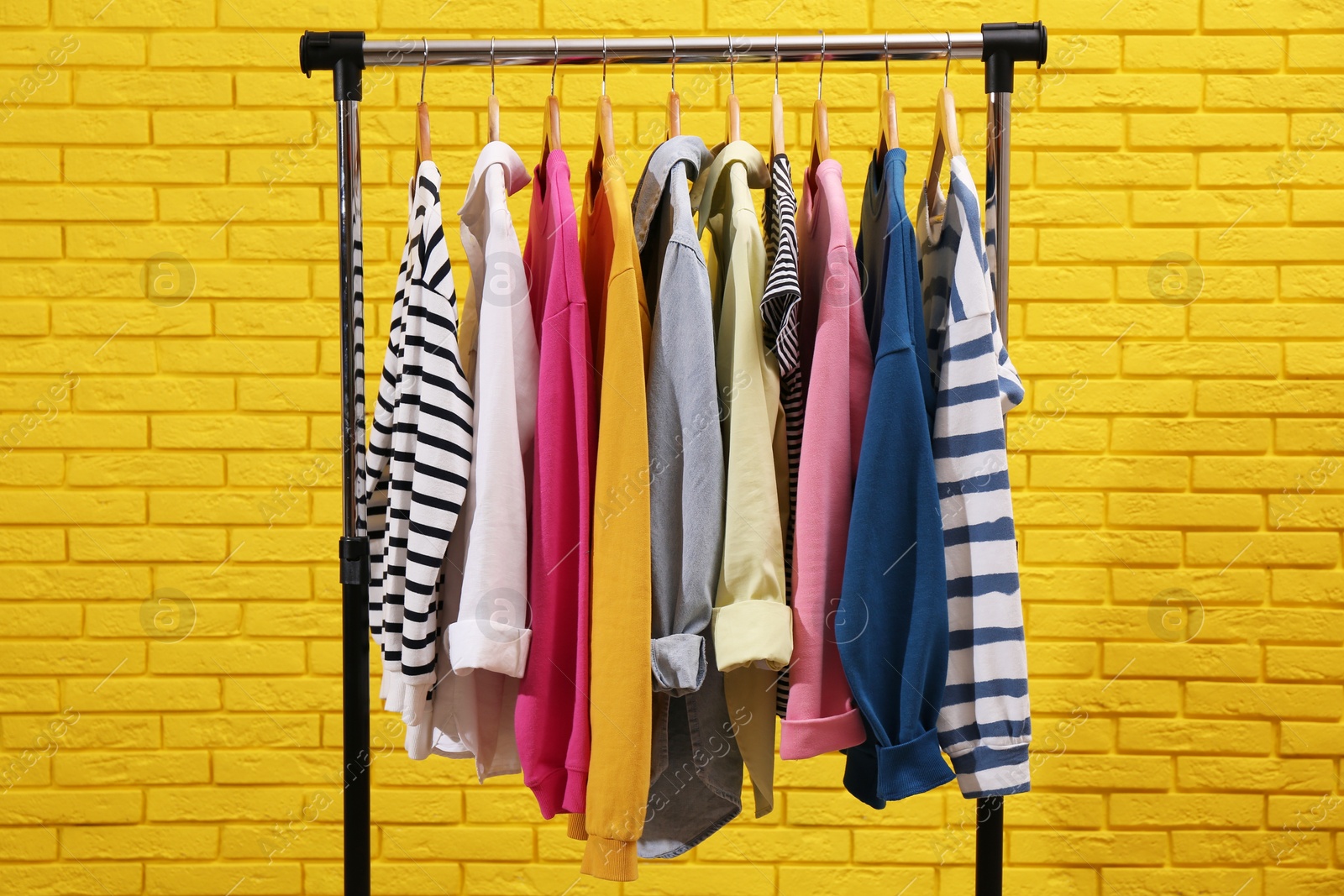 Photo of Rack with different stylish clothes near yellow brick wall