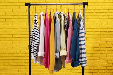 Rack with different stylish clothes near yellow brick wall