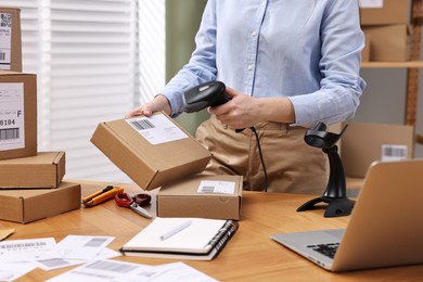 Photo of Parcel packing. Post office worker with scanner reading barcode at wooden table indoors, closeup