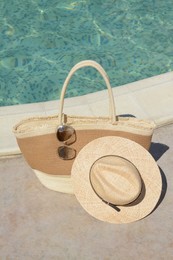 Photo of Stylish bag, sunglasses and hat near outdoor swimming pool on sunny day. Beach accessories