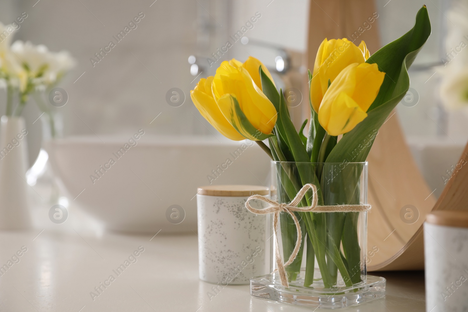 Photo of Beautiful yellow tulips near mirror on white table, closeup. Space for text