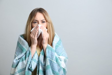 Photo of Young woman with blanket suffering from runny nose on light background. Space for text