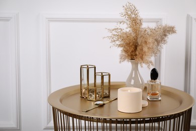 Photo of Burning soy candle, perfume and stylish accessories on table indoors. Space for text