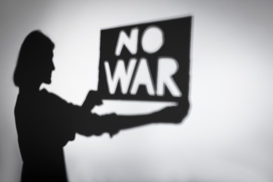 Photo of Shadow of woman holding poster with words No War on light background