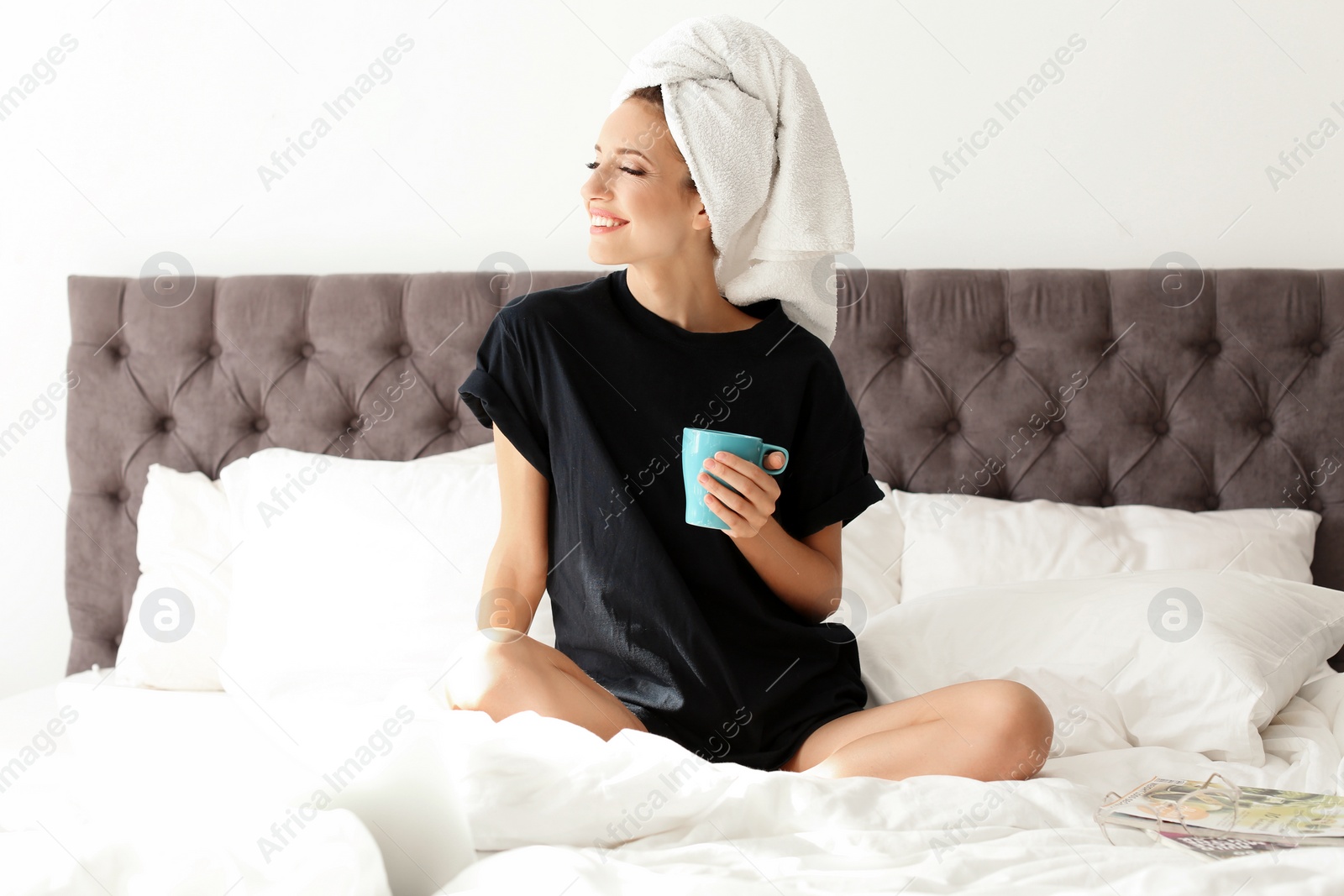 Photo of Beautiful young woman with cup of coffee sitting in bed at home. Lazy morning