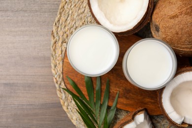 Photo of Glasses of delicious coconut milk, palm leaf and coconuts on wooden table, flat lay. Space for text