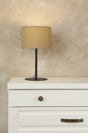Photo of Modern chest of drawers with lamp near beige wall