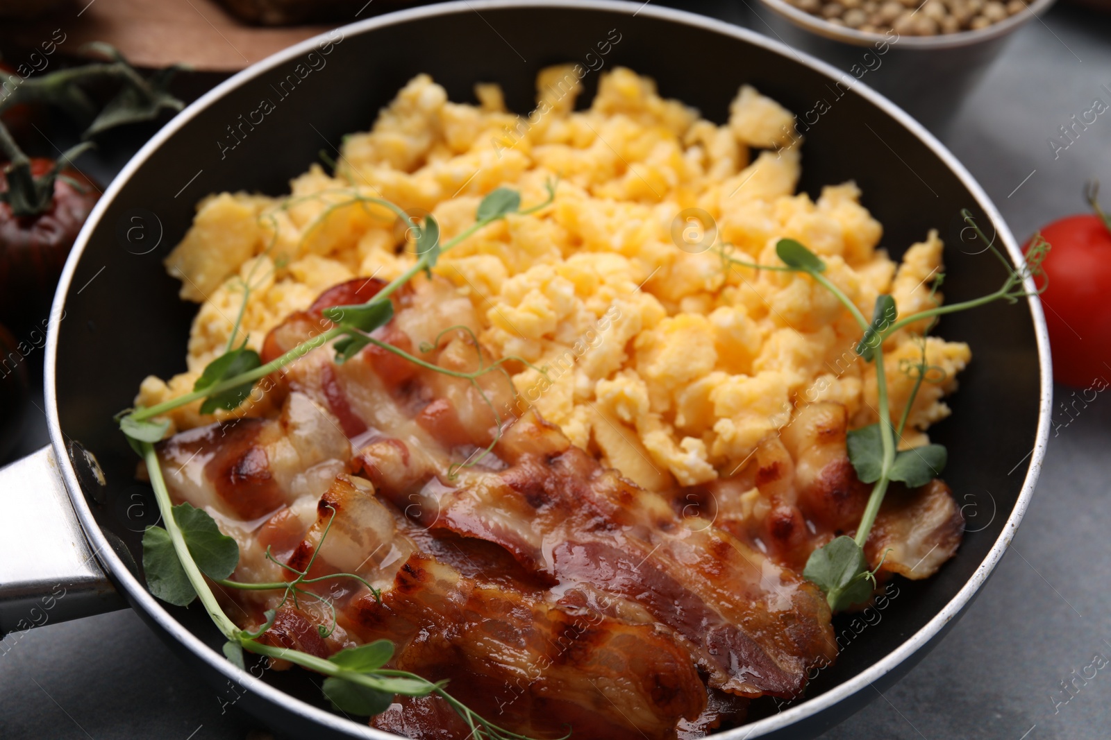 Photo of Delicious scrambled eggs with bacon in frying pan on grey table