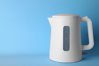 Modern electric kettle on light blue background, space for text