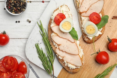 Photo of Board with delicious chicken bruschettas on white wooden table, flat lay