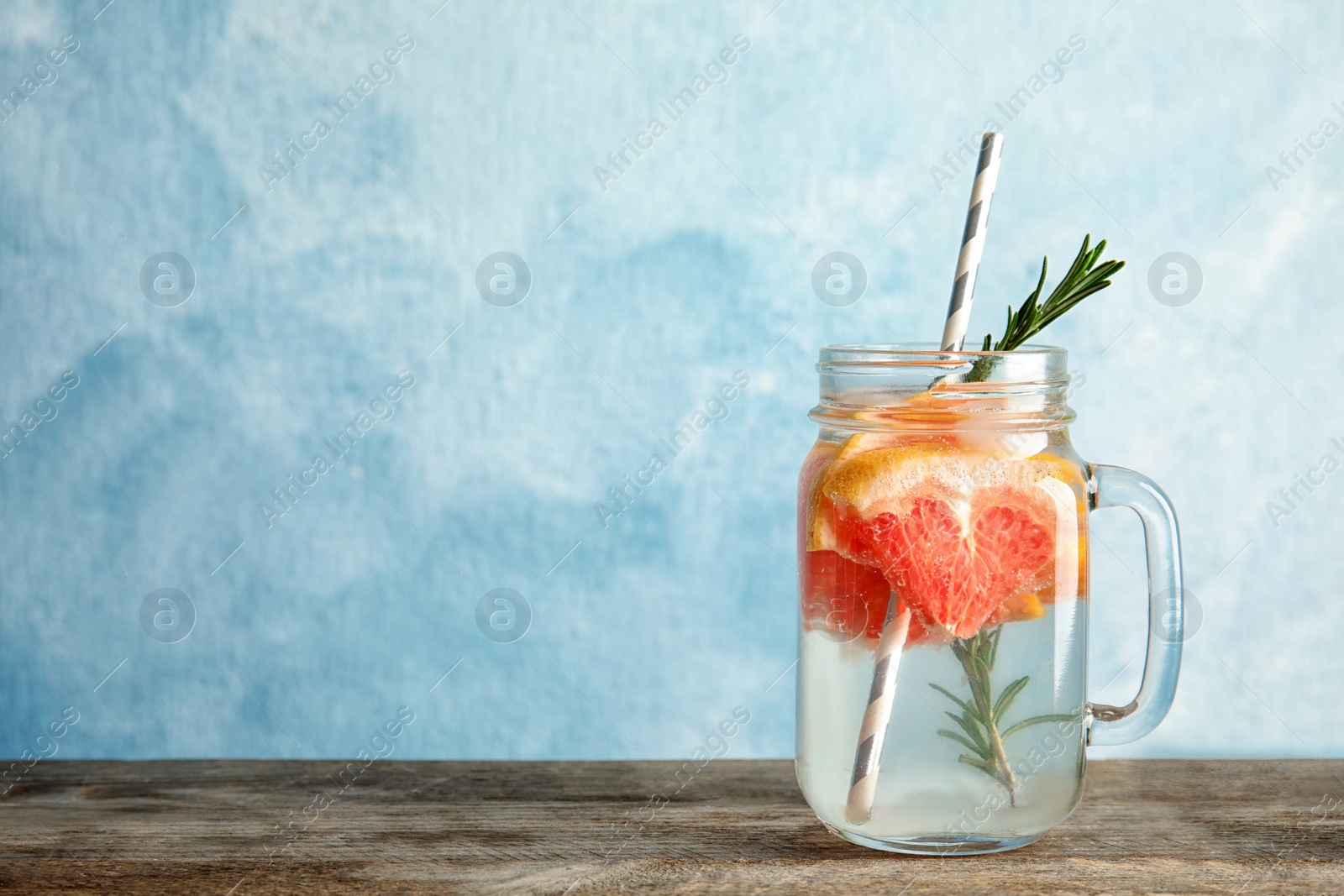 Photo of Mason jar of infused water with grapefruit slices on table against color background. Space for text