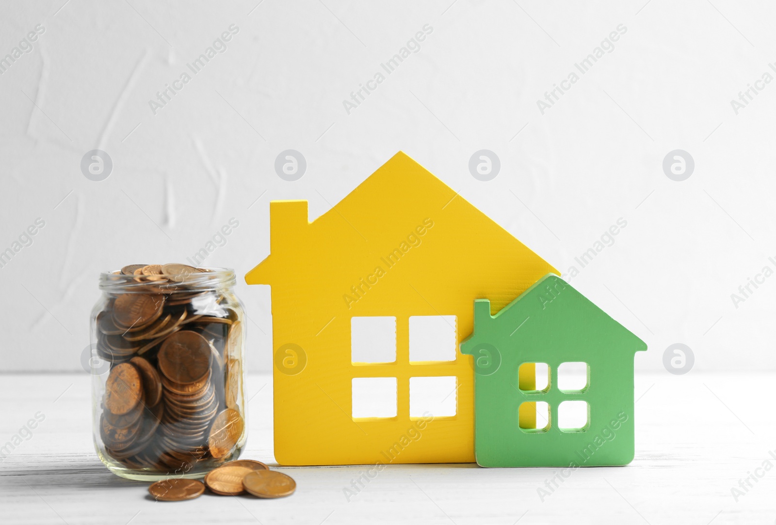 Photo of House figures and jar of coins on table against light background