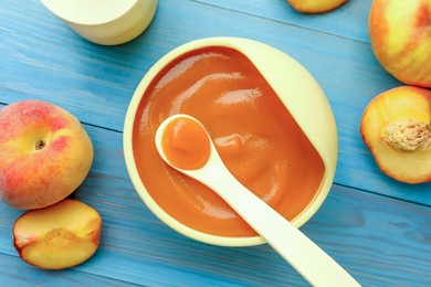 Photo of Bowl and spoon with tasty pureed baby food on light blue wooden table, flat lay