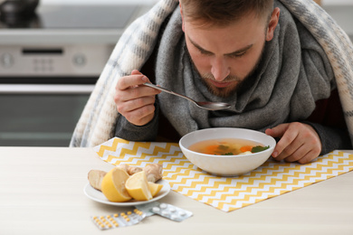 Photo of Sick young man eating tasty soup to cure flu at table in kitchen