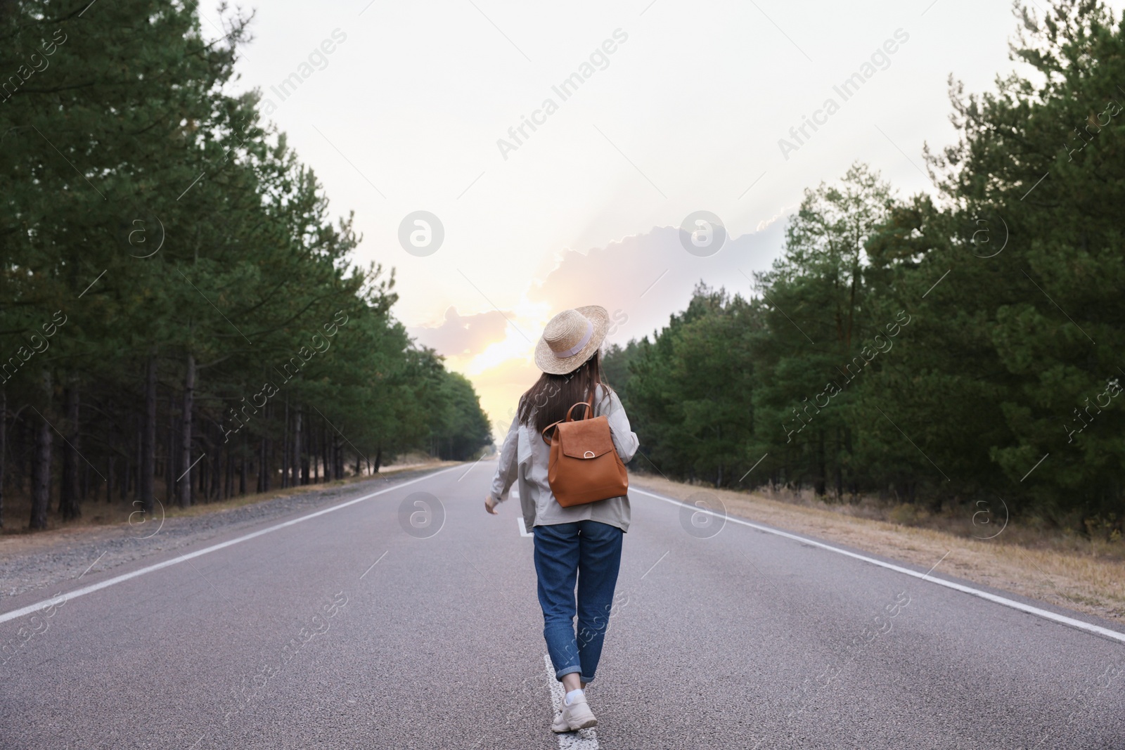 Photo of Young woman with stylish backpack walking along empty road, back view