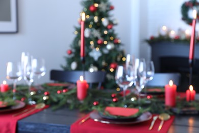 Elegant Christmas table setting with dishware and burning candles in festively decorated room, blurred view