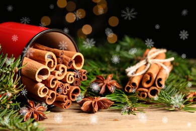 Cinnamon in red mug and anise surrounded by fir tree branches on wooden table, closeup