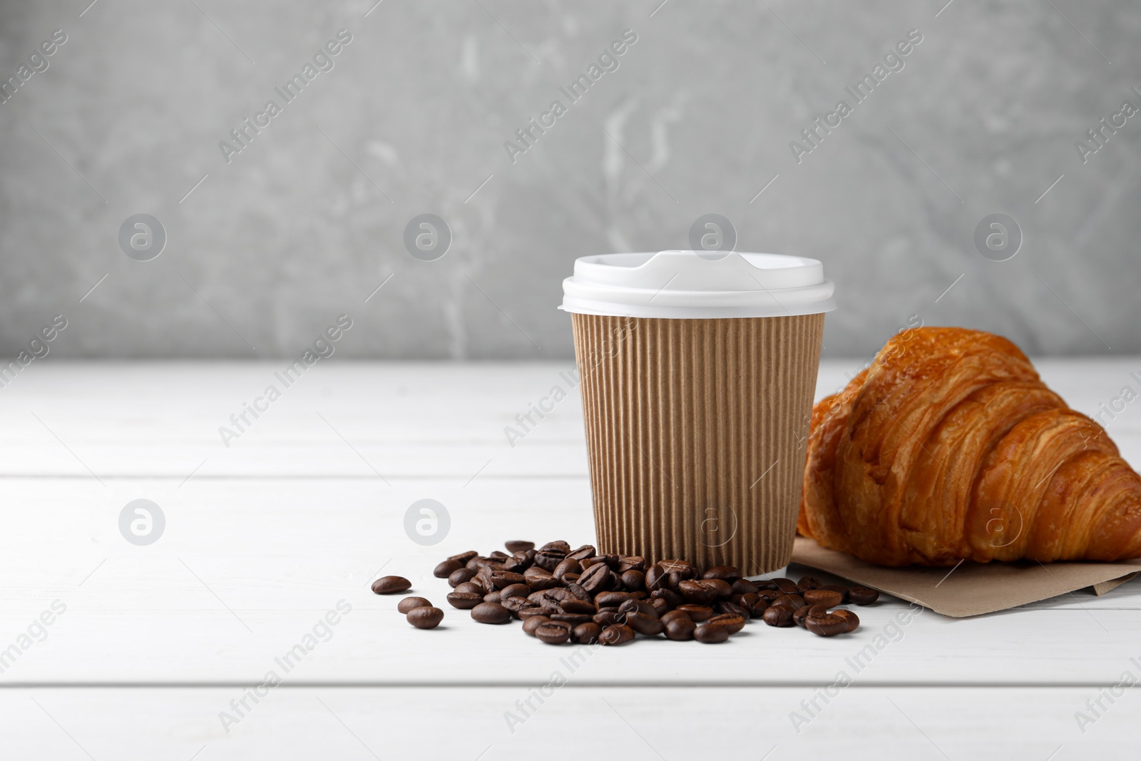 Photo of Coffee to go. Paper cup with tasty drink, croissant and beans on white wooden table. Space for text