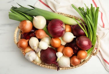 Photo of Wicker tray with fresh onion bulbs, leeks and garlic on white marble table, flat lay