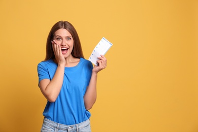 Photo of Portrait of excited young woman with lottery ticket on yellow background, space for text