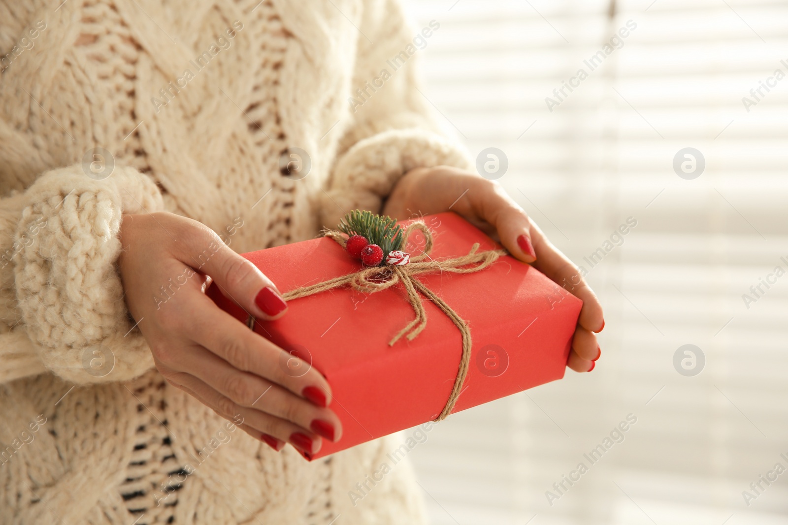 Photo of Woman holding red Christmas gift box indoors, closeup