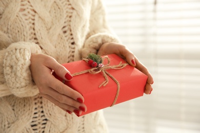 Woman holding red Christmas gift box indoors, closeup