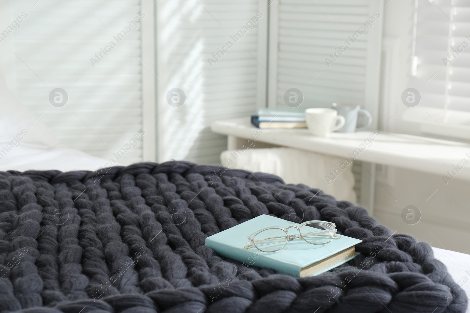 Photo of Book and glasses on knitted merino wool plaid in bedroom, space for text