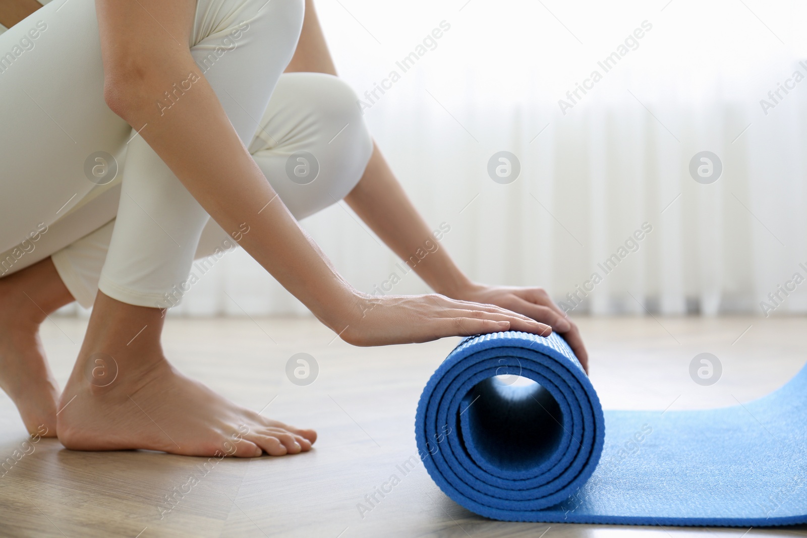 Photo of Woman rolling blue yoga mat indoors, closeup