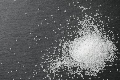 Photo of Heap of granulated sugar on black table, top view. Space for text