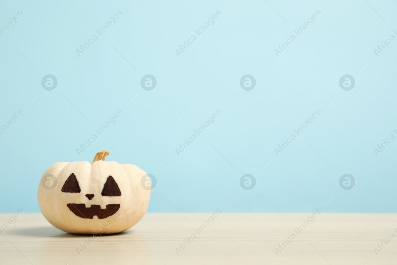 Photo of Pumpkin with scary face on light blue background, space for text. Halloween decor