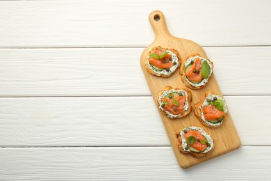 Photo of Tasty canapes with salmon, capers, cucumber and sauce on white wooden table, top view. Space for text