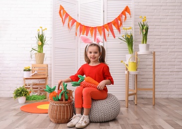 Photo of Adorable little girl with bunny ears and toy carrots in Easter photo zone