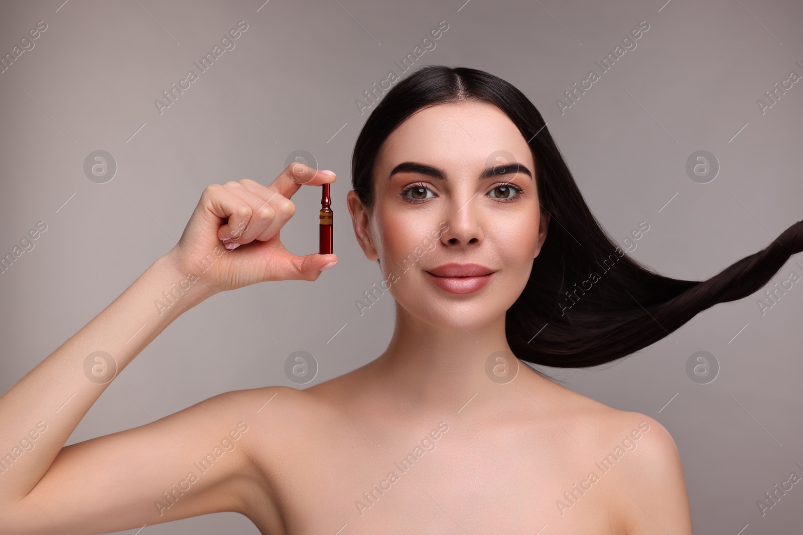 Photo of Beautiful young woman with long healthy hair holding ampoule on grey background