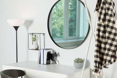 Stylish round mirror on white wall over desk in room