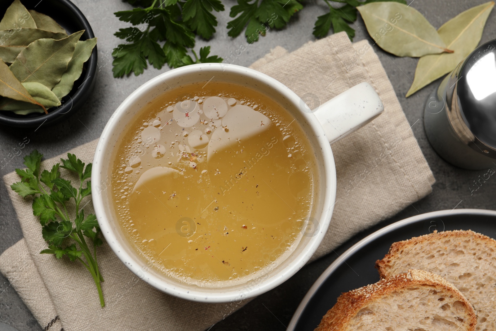 Photo of Hot delicious bouillon in cup on grey table, flat lay