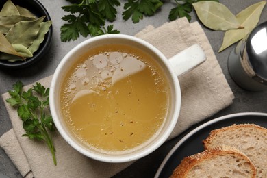 Photo of Hot delicious bouillon in cup on grey table, flat lay