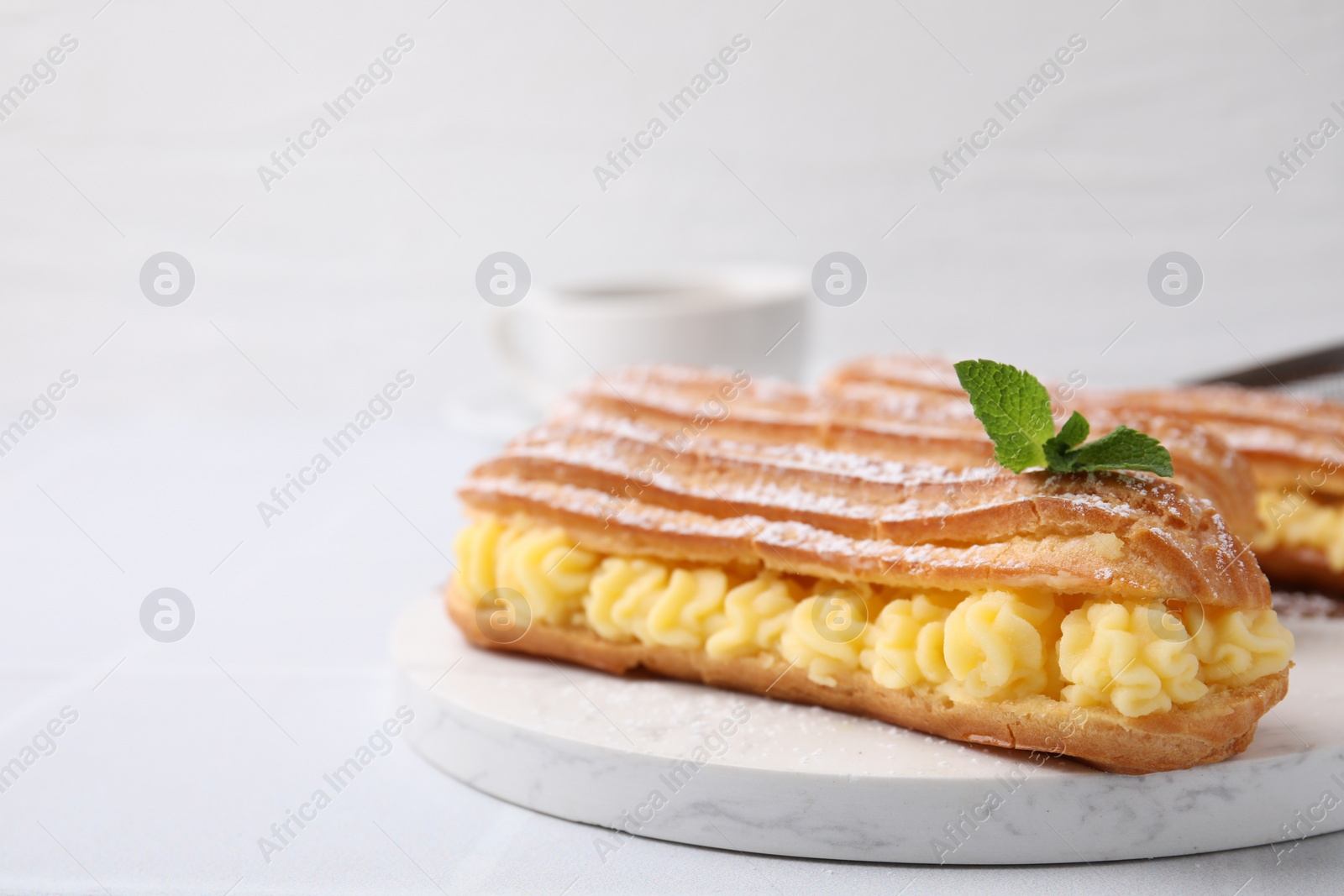 Photo of Delicious eclairs filled with cream and mint on white table, closeup. Space for text