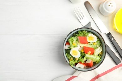 Photo of Delicious salad with crab sticks and eggs in bowl on white wooden table, flat lay. Space for text