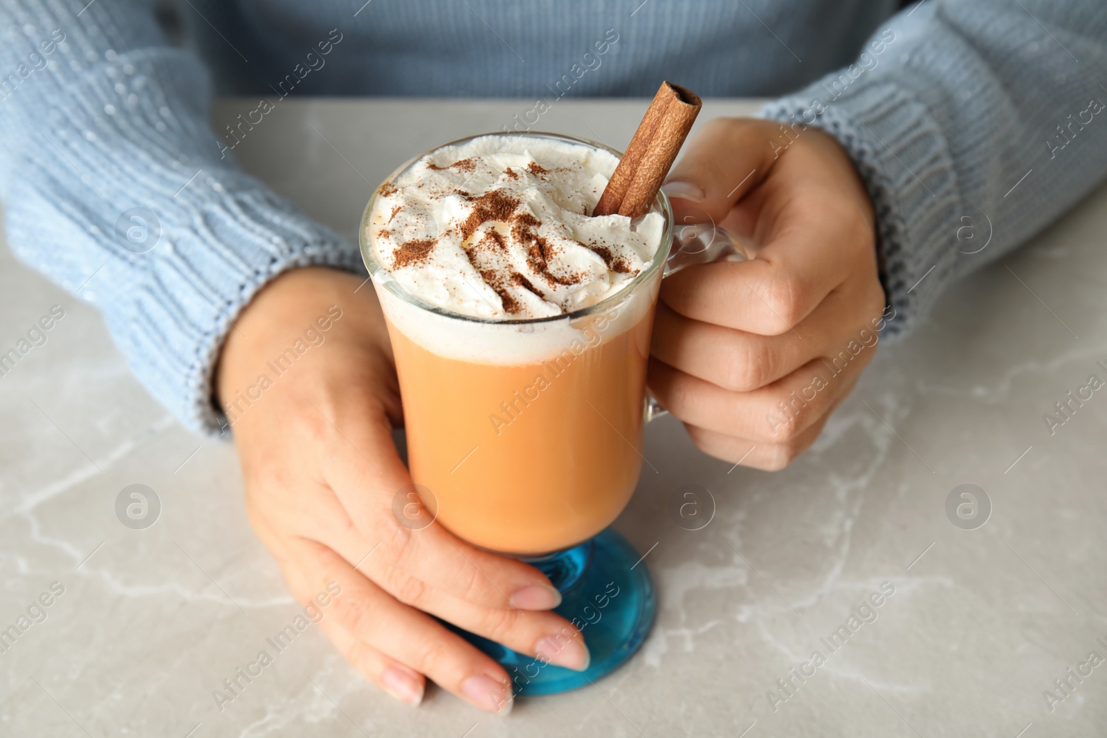 Photo of Woman holding glass cup with pumpkin spice latte and whipped cream on light table