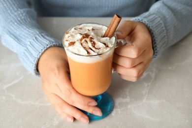 Photo of Woman holding glass cup with pumpkin spice latte and whipped cream on light table