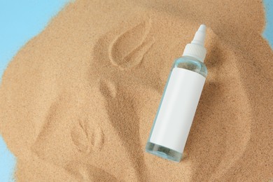 Photo of Bottle with serum on sand against light blue background, top view and space for text. Cosmetic product