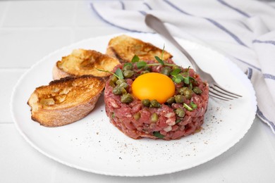 Photo of Tasty beef steak tartare served with yolk, capers and toasted bread on white table