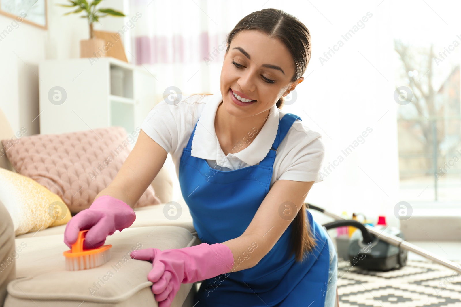 Photo of Portrait of woman cleaning sofa with brush in living room