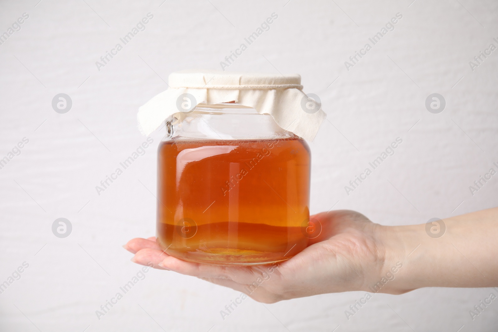 Photo of Woman holding glass jar of tasty kombucha on white background, closeup