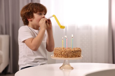 Photo of Birthday celebration. Cute boy with party blower at table with tasty cake indoors